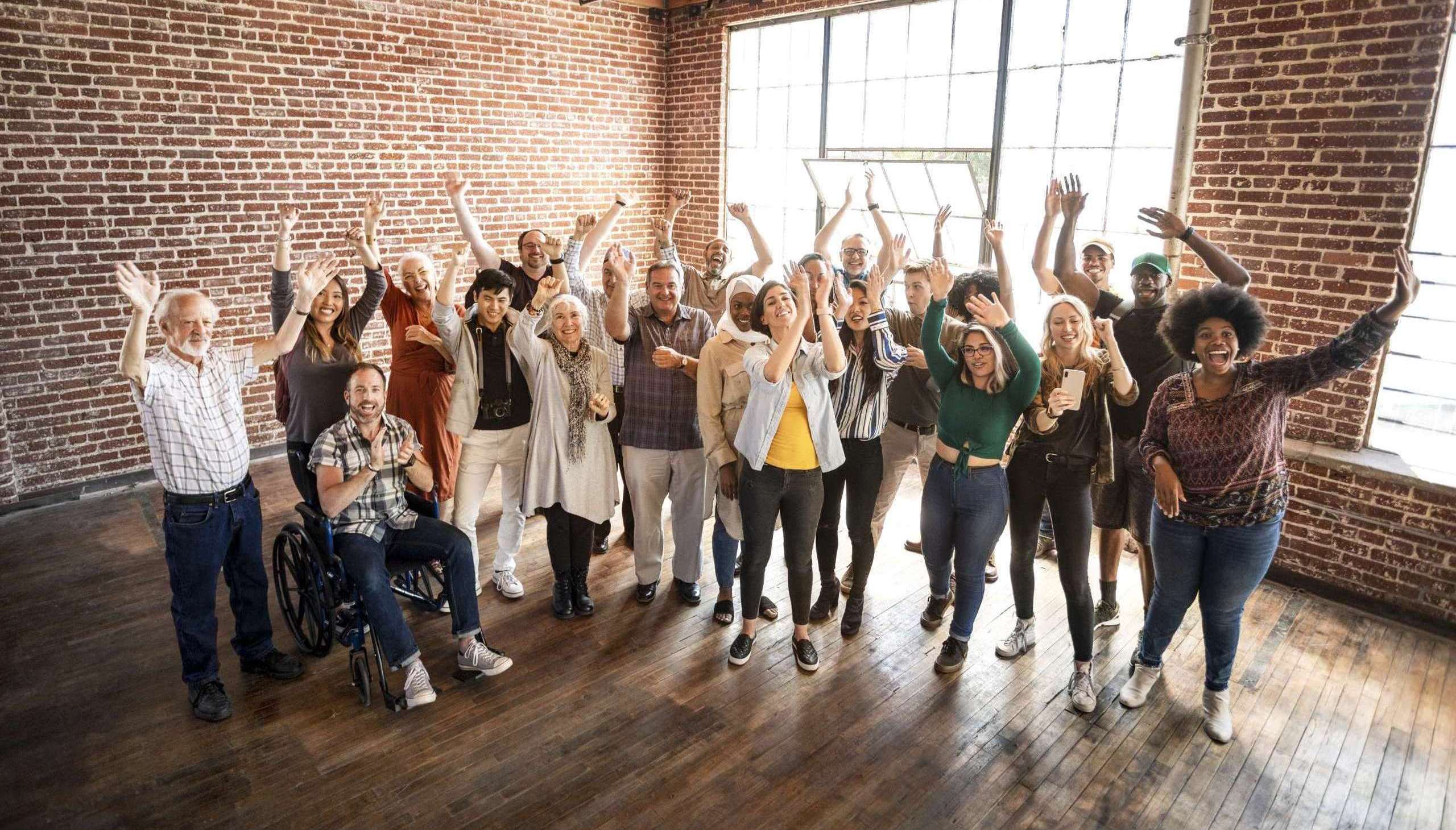 Diverse group of people celebrating in a loft-style room with hands raised.