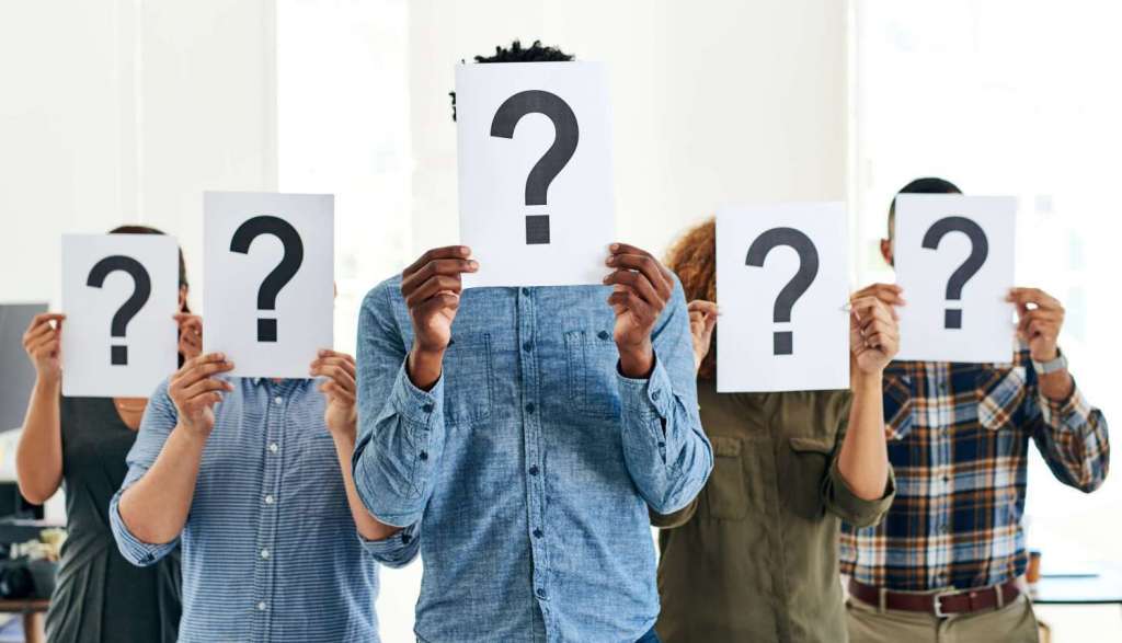 A diverse group of people holding up sheets of paper with large question marks covering their faces.