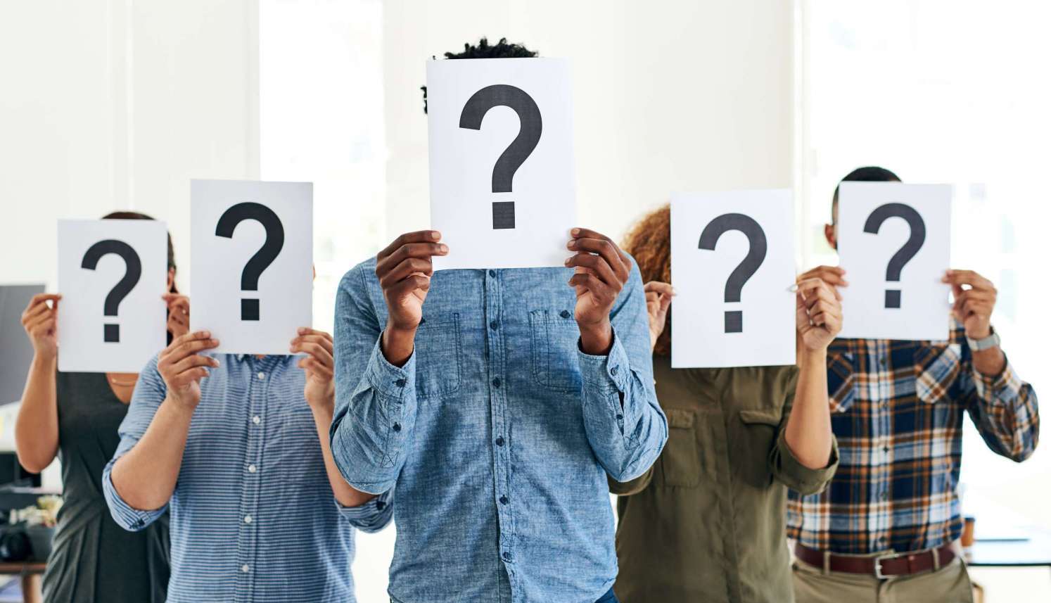 A diverse group of people holding up sheets of paper with large question marks covering their faces.