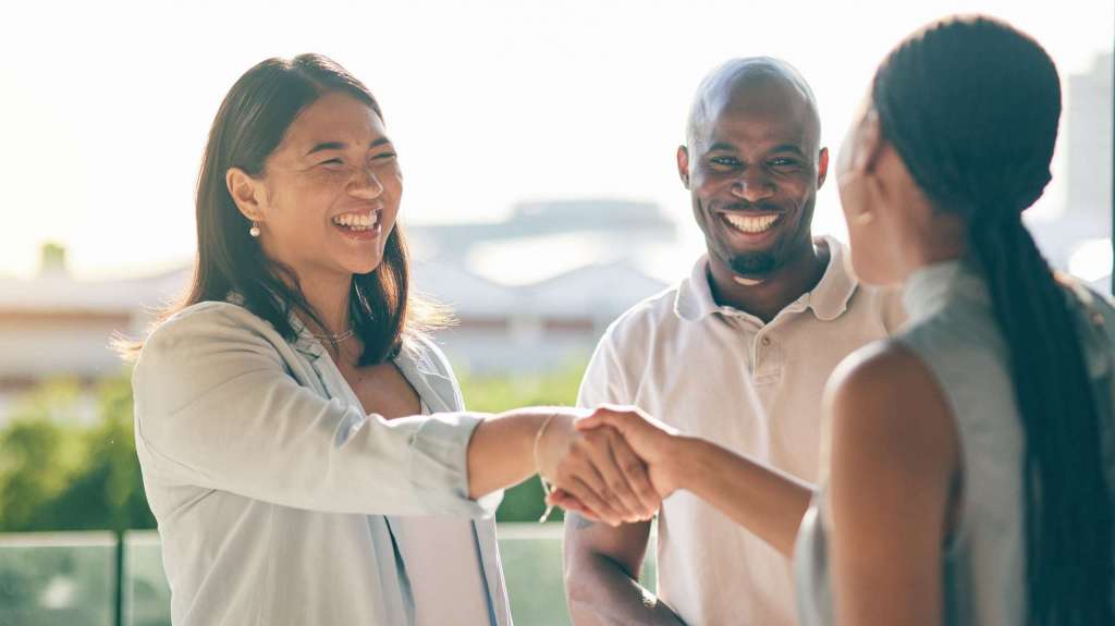 A diverse group of professionals smiling and shaking hands outdoors during a business meeting, symbolizing collaboration and positive partnership.