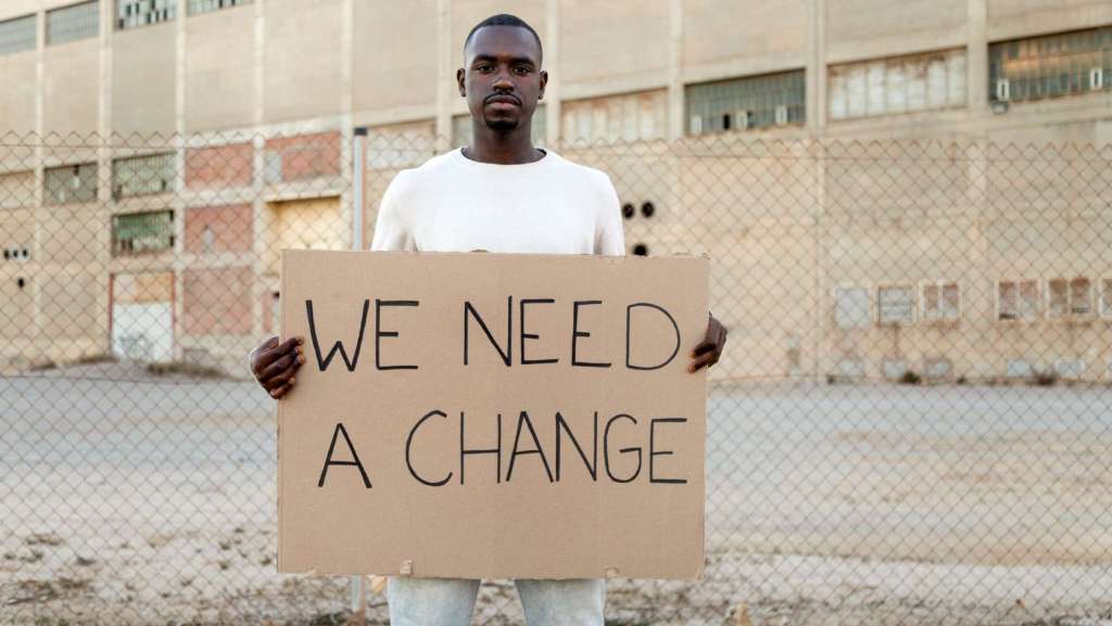 African American man holding a cardboard sign that says “We Need a Change,” symbolizing the need for church evolution and renewal.