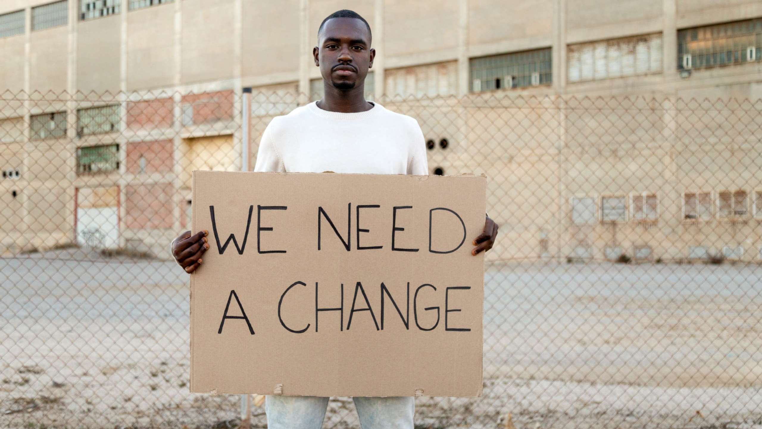 African American man holding a cardboard sign that says “We Need a Change,” symbolizing the need for church evolution and renewal.