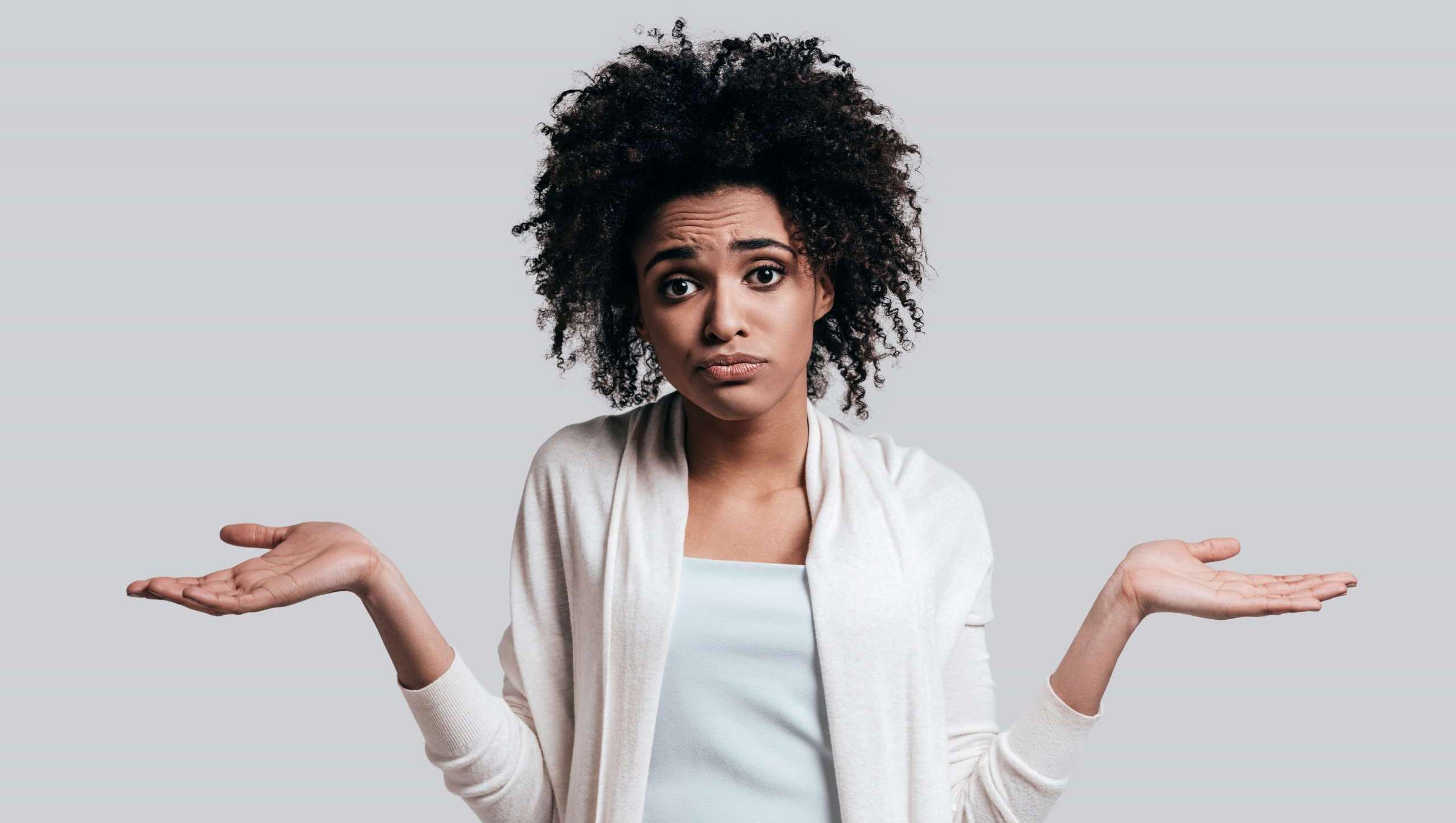 Confused young woman shrugging with both hands raised, symbolizing uncertainty or mixed messages