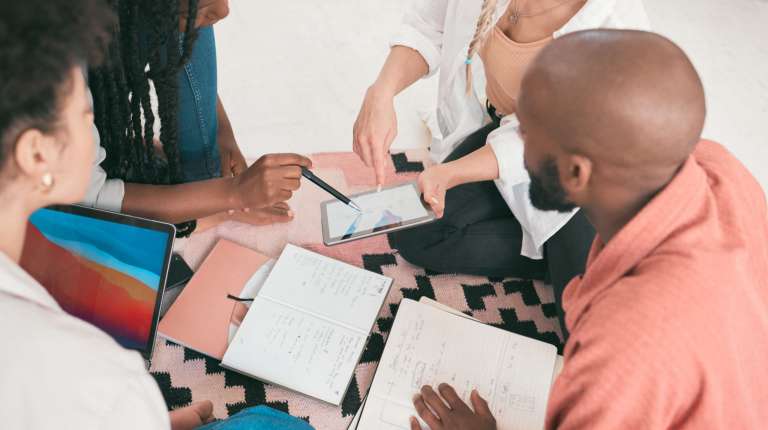 A diverse group of church team members sitting together with notebooks and a tablet, planning their communication and marketing strategy in a relaxed, collaborative setting.